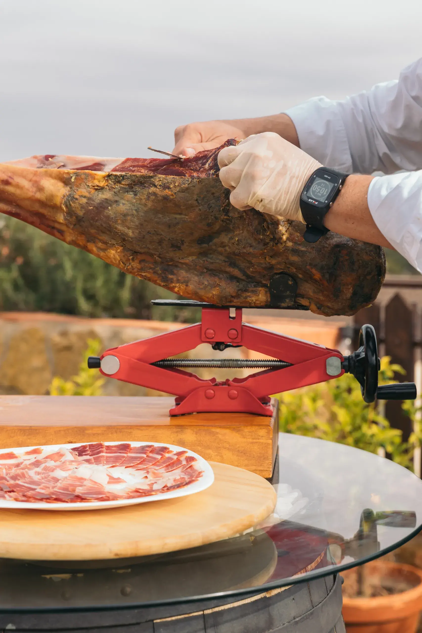 Manos con guantes cortando la maza sobre el soporte, con el plato de lonchas delante